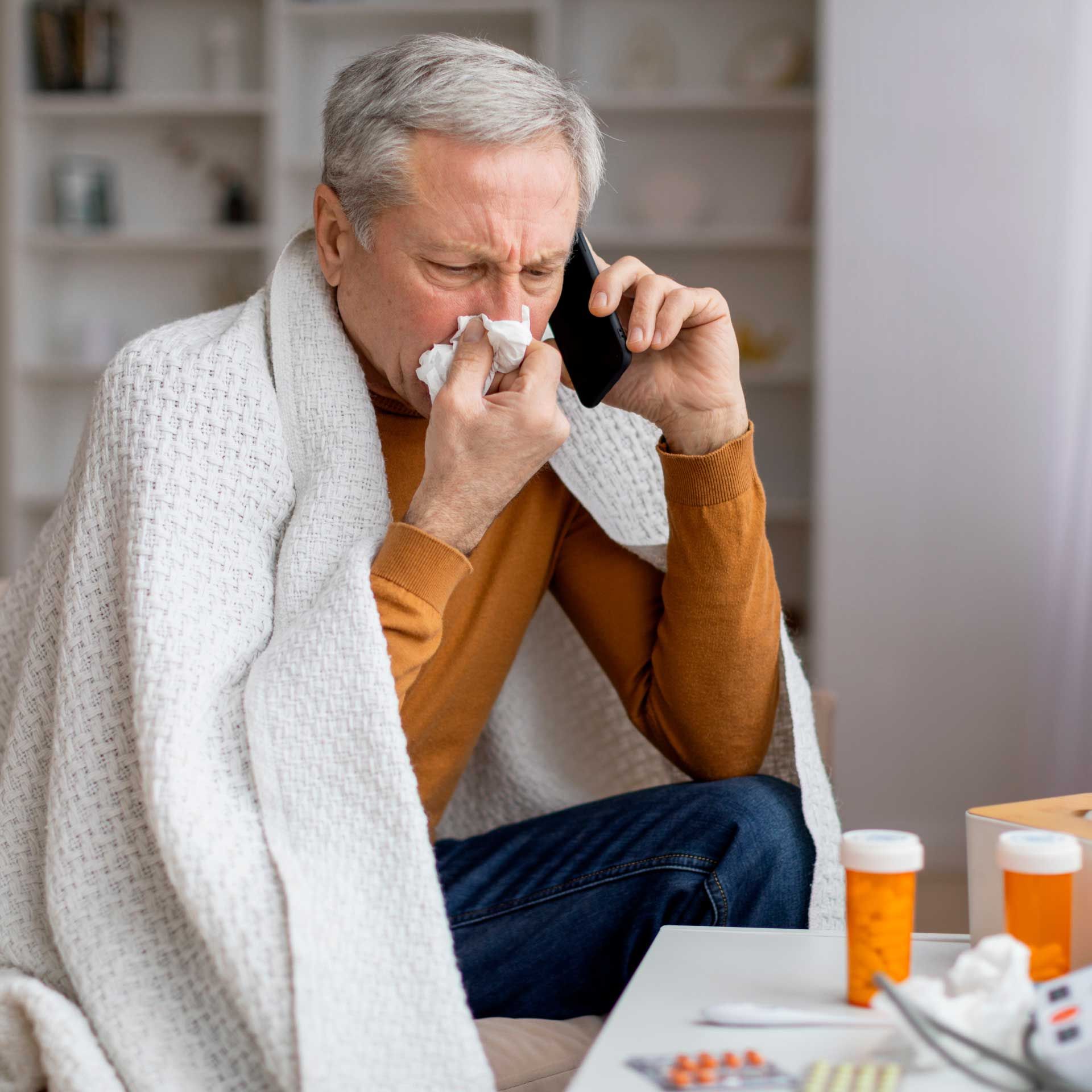 Older man sitting at computer coughing sick on telemed video call