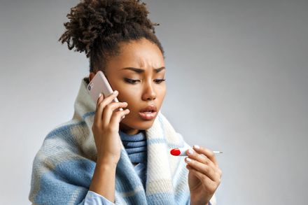 Safewell Personal Safety and Wellness App. A woman wrapped in a blanket is holding a thermometer and talking on a cell phone.