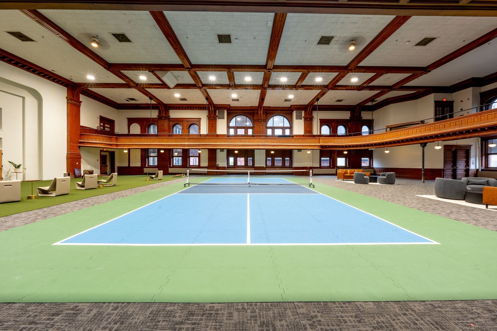 Indoor pickleball court with blue and green flooring, surrounded by seating and a wooden balcony at Zenith Apartments in Duluth, MN.