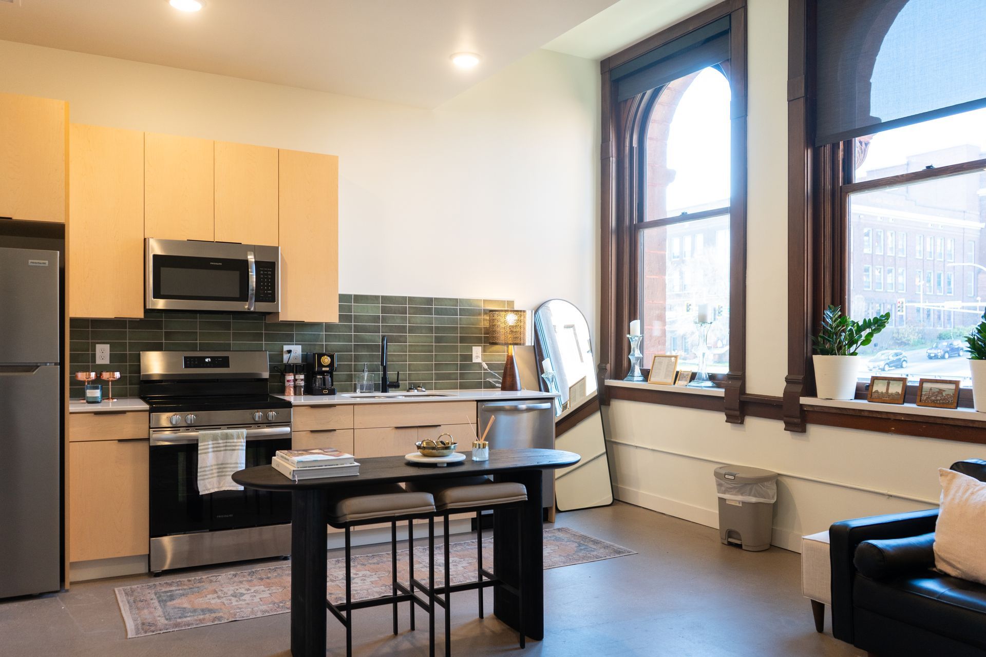 Modern kitchen and living space with natural light. Includes a table, stools, and a black leather chair.