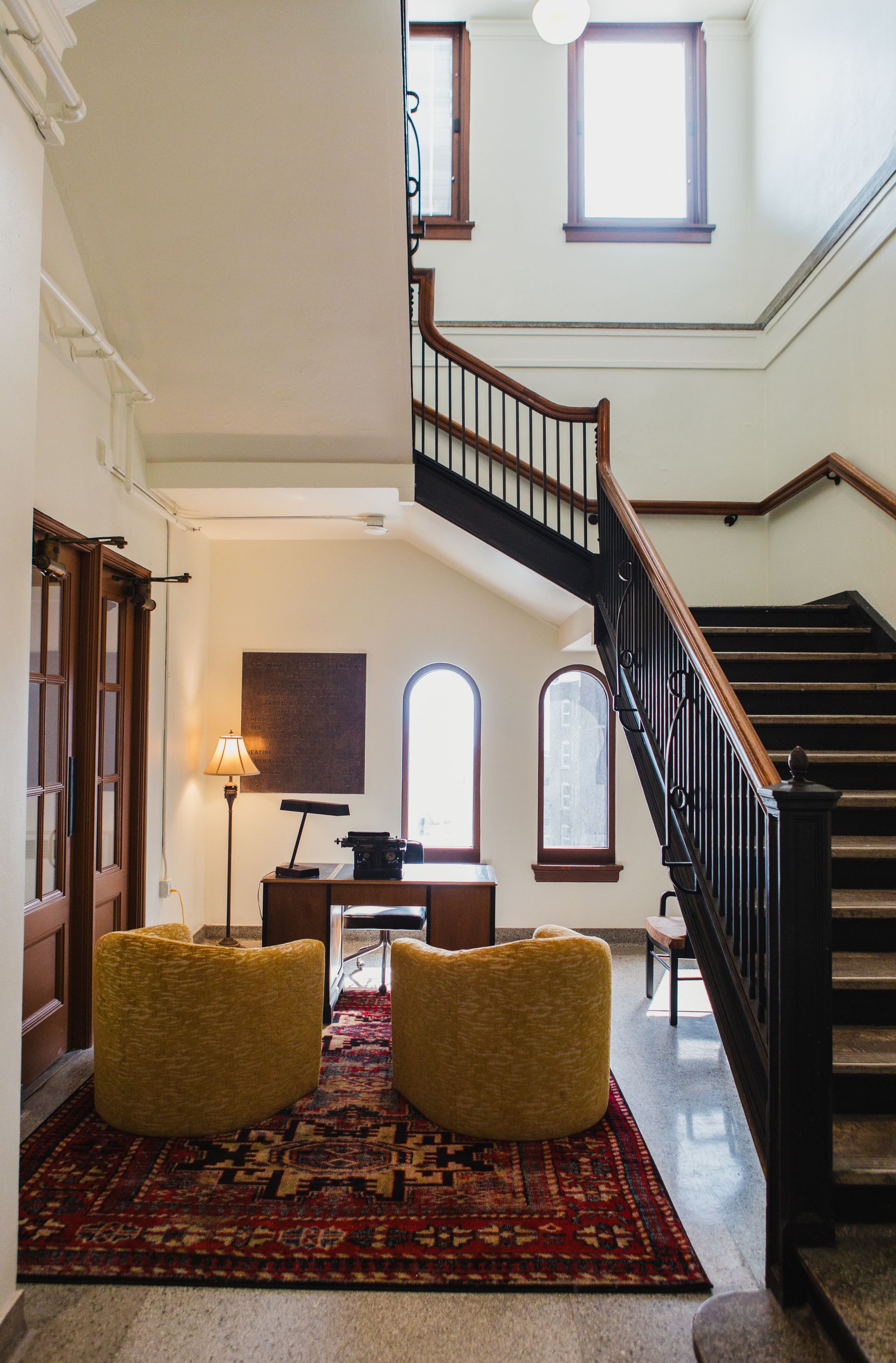 Staircase in a building with a desk, two yellow chairs, and a rug.