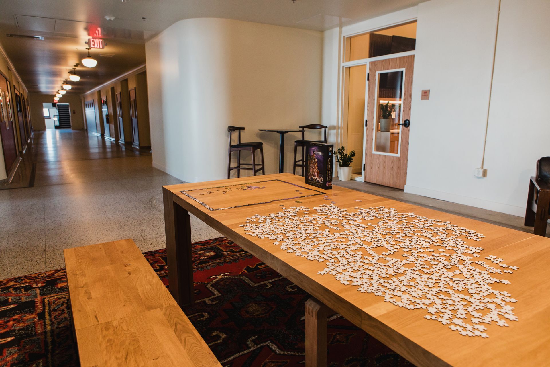 Long hallway with a table covered in a partially completed puzzle, and a bench.