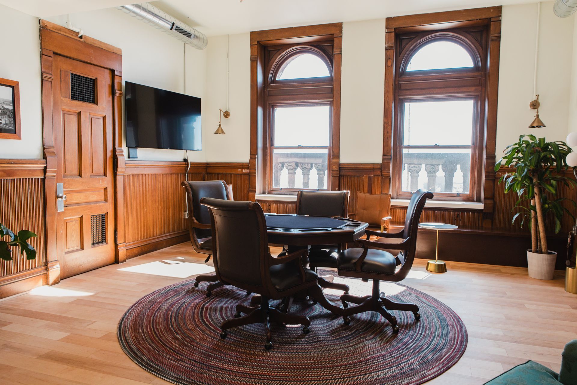 Elegant room with wooden paneling, poker table, leather chairs, and arched windows.