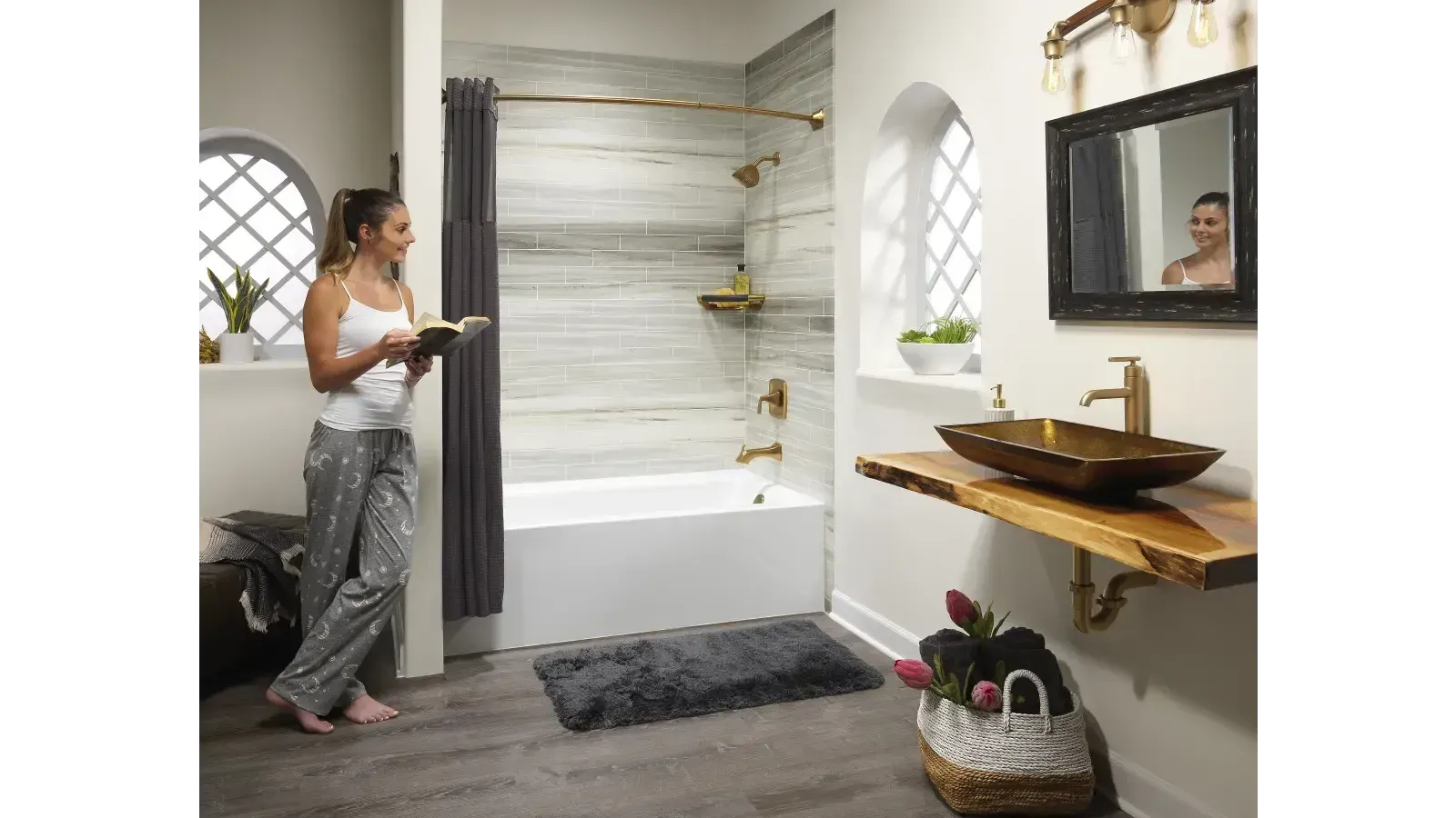 Woman standing in a modern bathroom beside a white bathtub, holding a phone, with mirror and vanity nearby