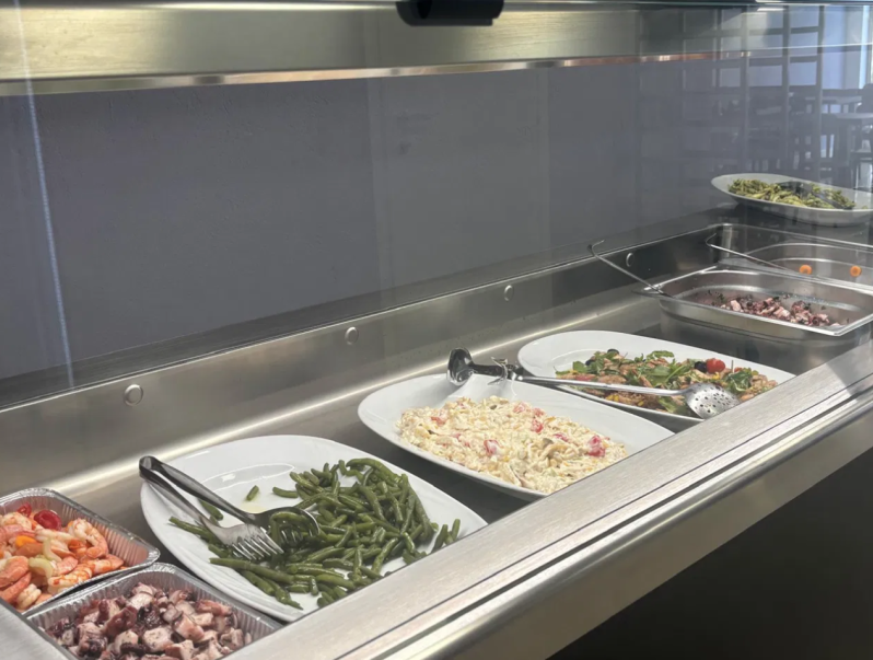 Prosciutti stagionati appesi in una rete al banco di un mercato, con un prosciutto grande al centro sopra gli altri