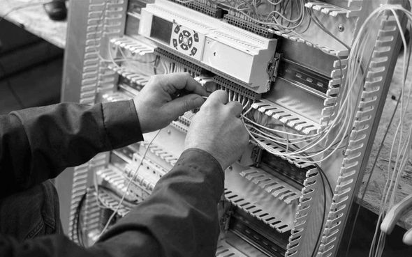 Hands wiring a network panel with rows of cables and connectors