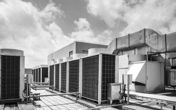 Rooftop HVAC units and ducts in black and white under a cloudy sky