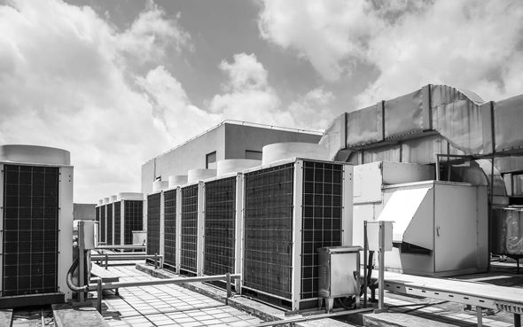 Rooftop HVAC units and ductwork under a cloudy sky on an industrial building