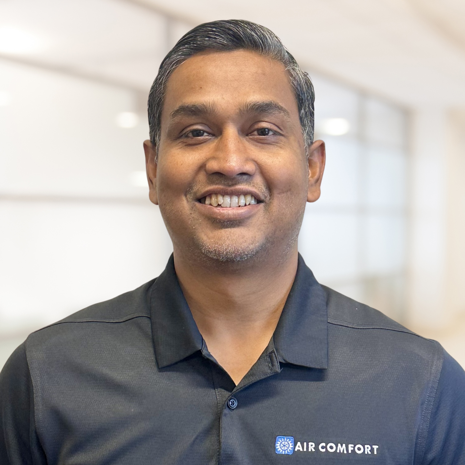 Smiling person in a navy shirt against a bright blurred office background