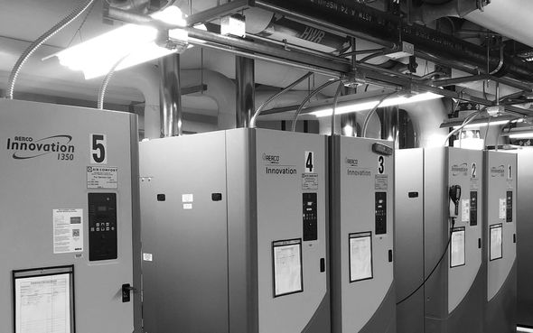 Row of industrial electrical cabinets in a factory or utility room, with pipes and ducts overhead.