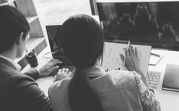 Two coworkers discussing charts on a computer monitor in an office setting