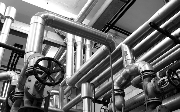Industrial pipes and valves overhead in a mechanical plant, with shiny metal ductwork and handwheels.