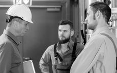 Three workers in hard hats and safety gear talking in an industrial setting