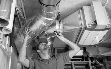 Technician inspecting overhead HVAC ductwork in a mechanical room