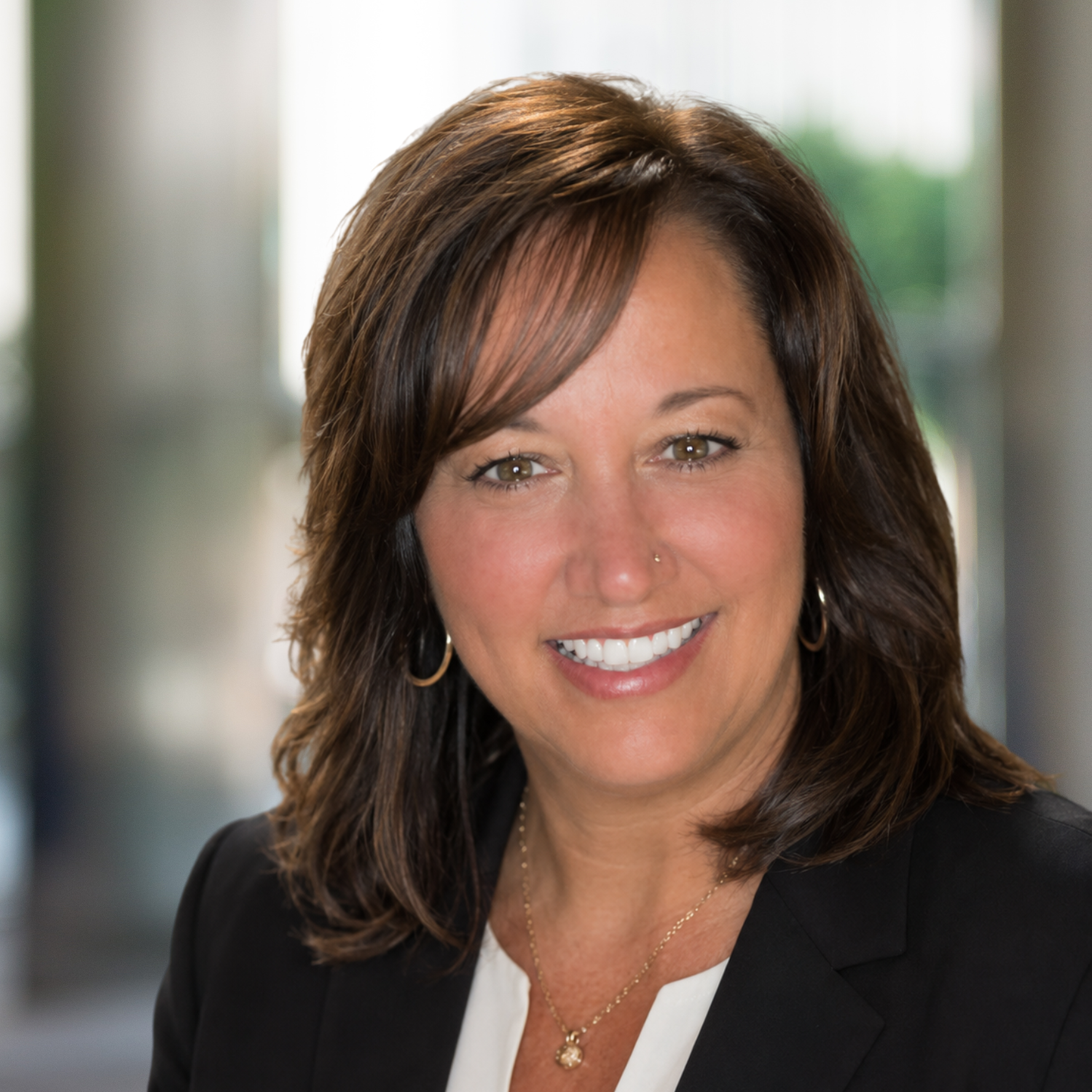 Smiling professional portrait in black blazer and white blouse, with a blurred office background