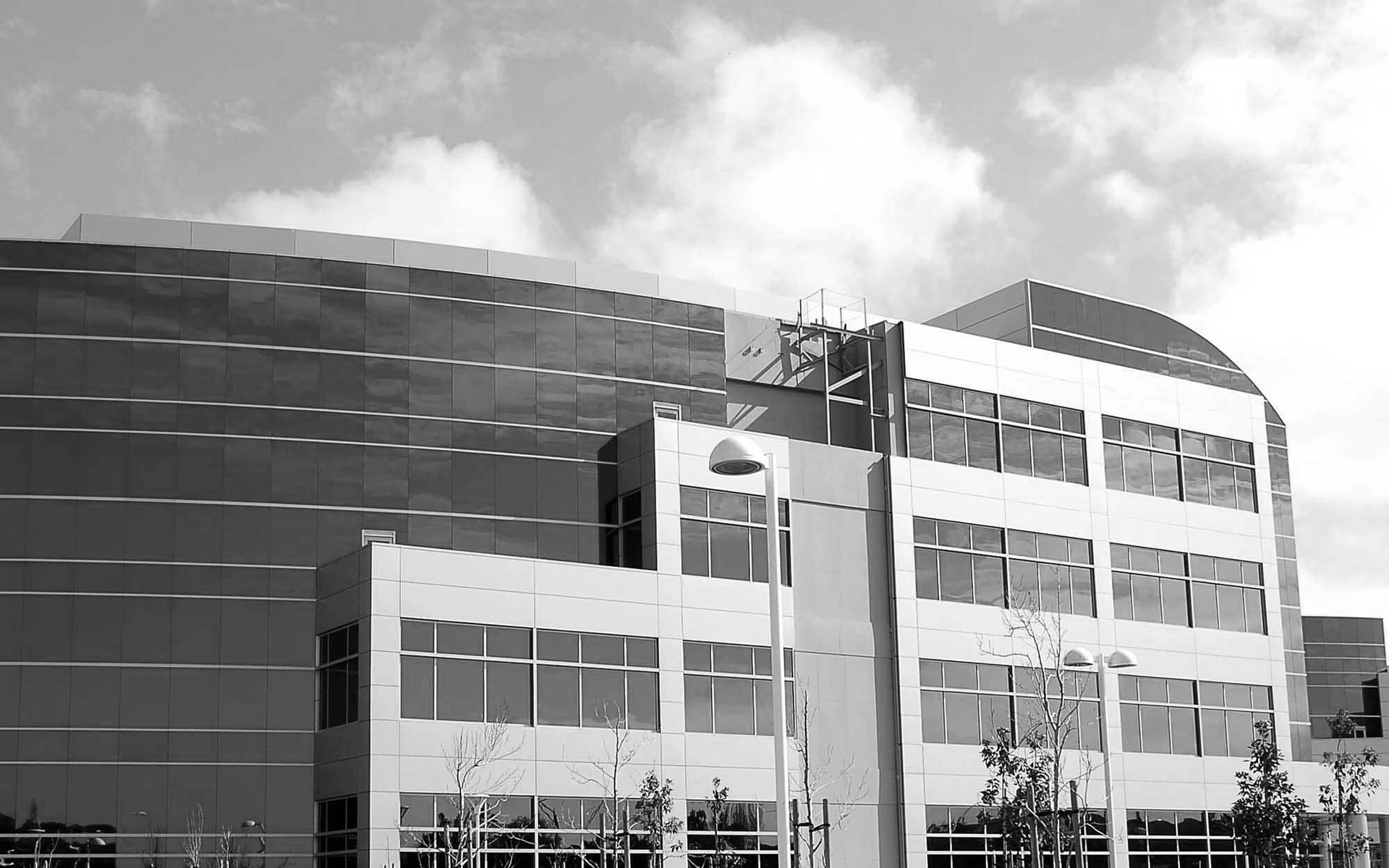 Modern office building with glass windows and a dark curved facade under a cloudy sky