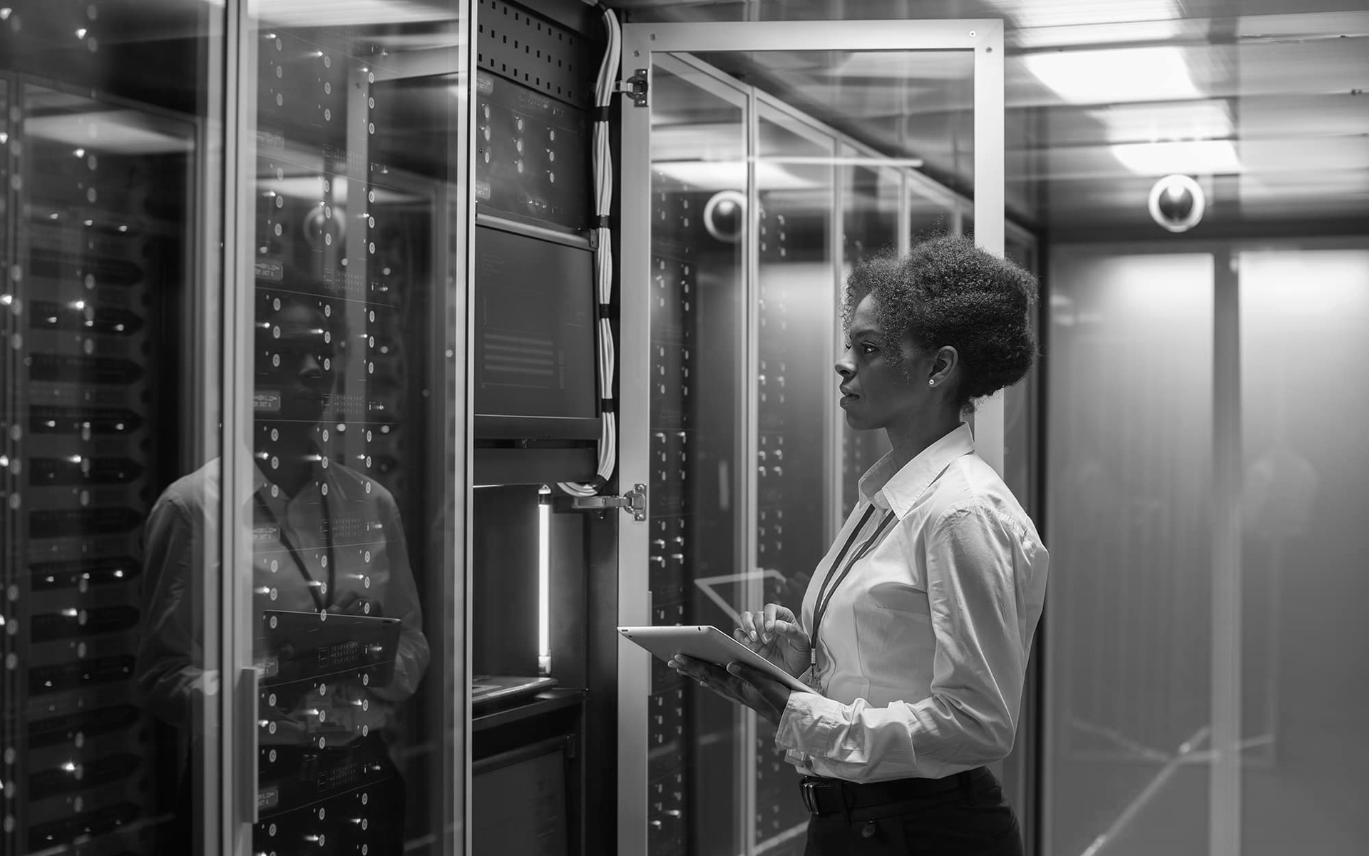 Person holding a tablet beside server racks in a data center