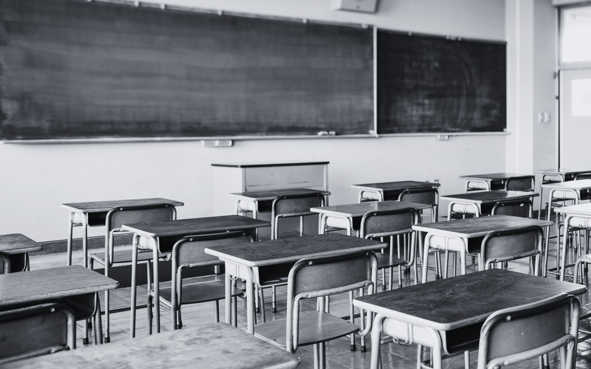Empty classroom with desks and chairs facing a chalkboard and teacher’s desk