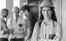 Factory worker in hard hat standing in an industrial setting, with colleagues blurred in the background