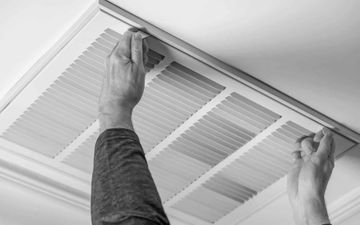 Hands installing or cleaning a ceiling air vent grille with a screwdriver.