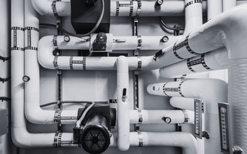 White industrial pipes and valves on a wall, with a pressure gauge and cable connection.