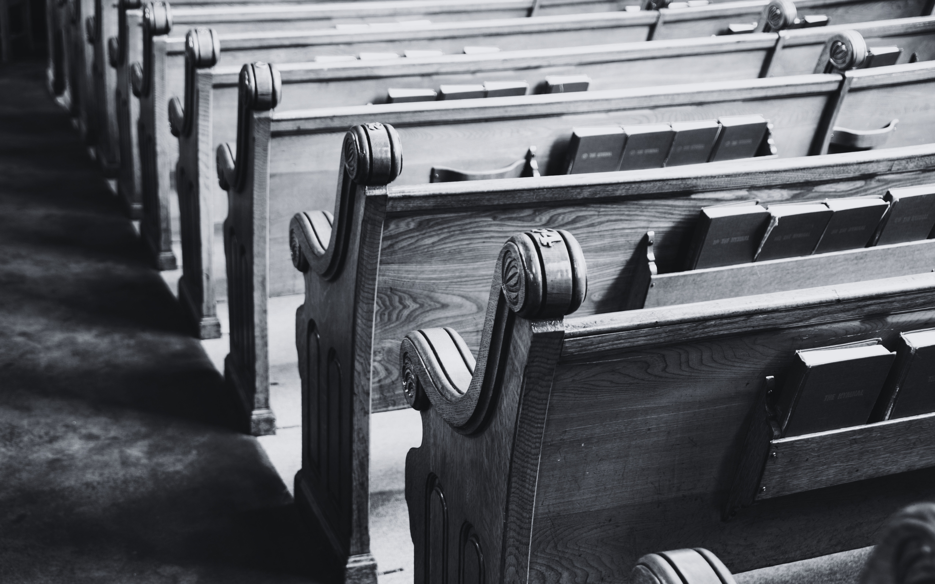 Black-and-white photo of empty church pews in a row, viewed from the aisle
