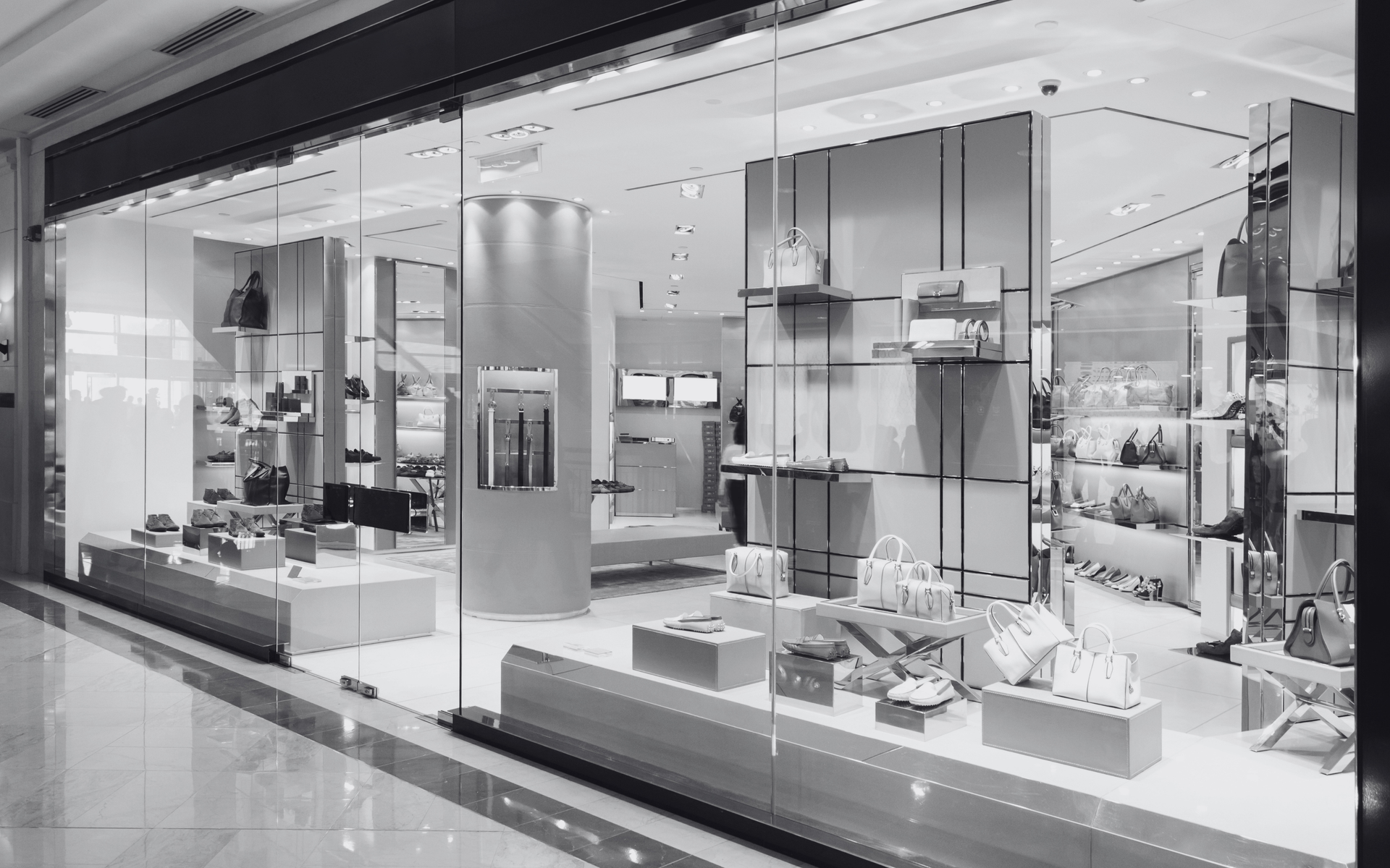 Luxury storefront display with glass shelves, handbags, and decor in a bright mall corridor