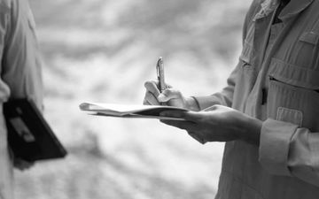 Person holding a notepad and pen, writing outdoors in a blurred black-and-white scene