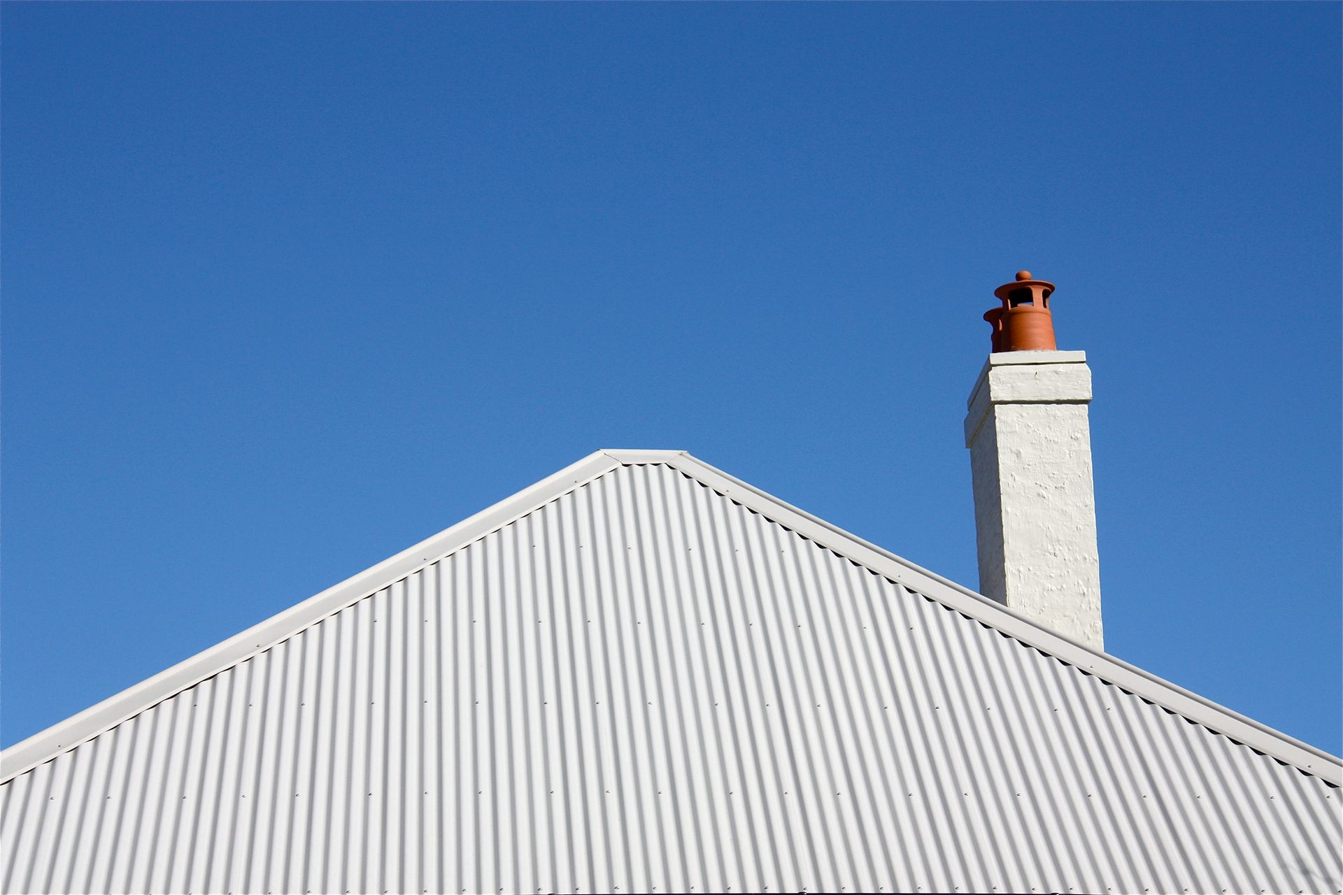 White corrugated metal roof with a chimney against a blue sky.