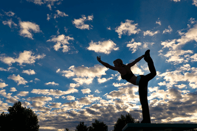 A person in silhouette performs a standing yoga pose against a cloudy, sunset-lit sky.
