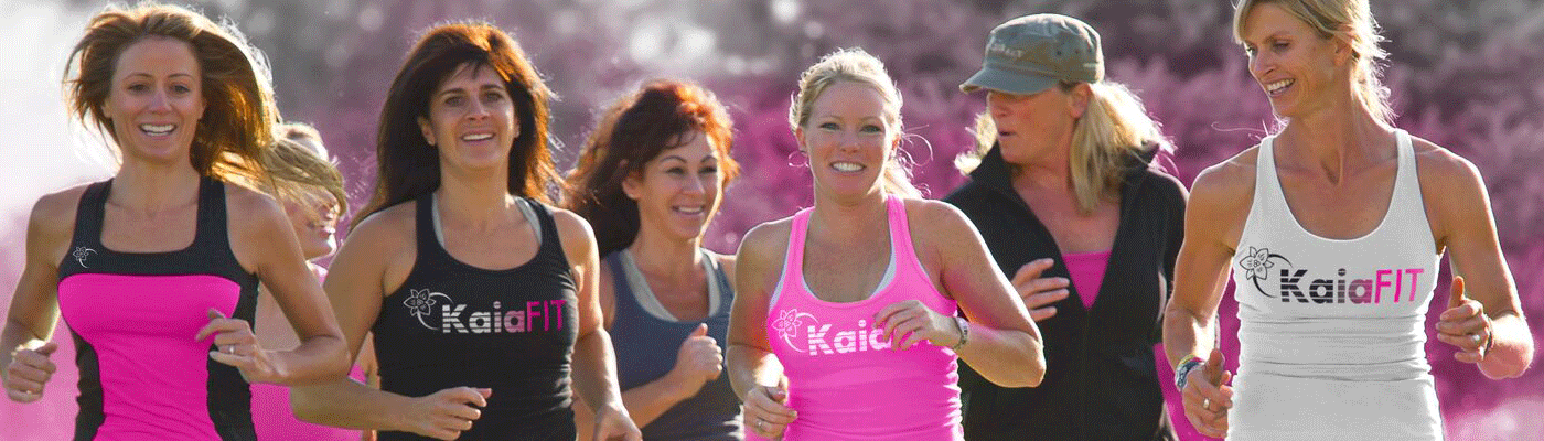 A group of people wearing athletic gear jog outdoors, smiling as they run together against a soft, pink-toned background.