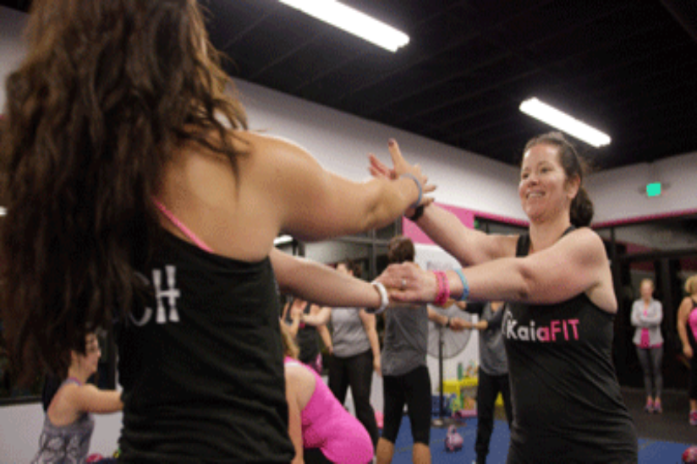 Two people in a gym smiling and holding hands while facing each other during a workout class.