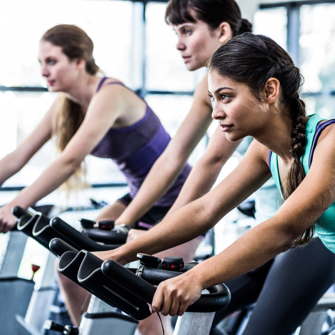 Three individuals exercising on stationary bikes in a gym, focusing on their workout with serious expressions.