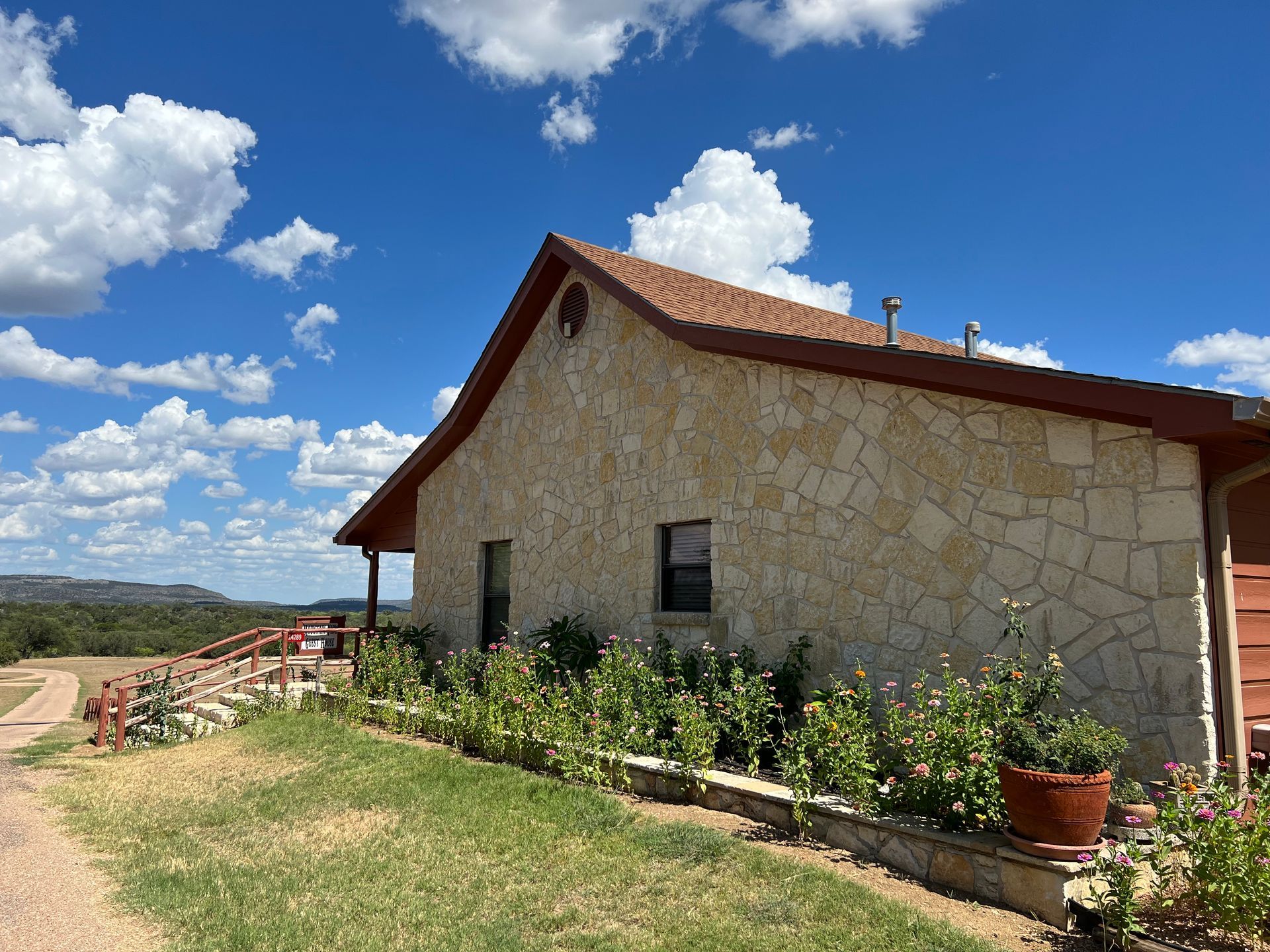 A large stone house with a red roof is sitting on top of a lush green hillside.