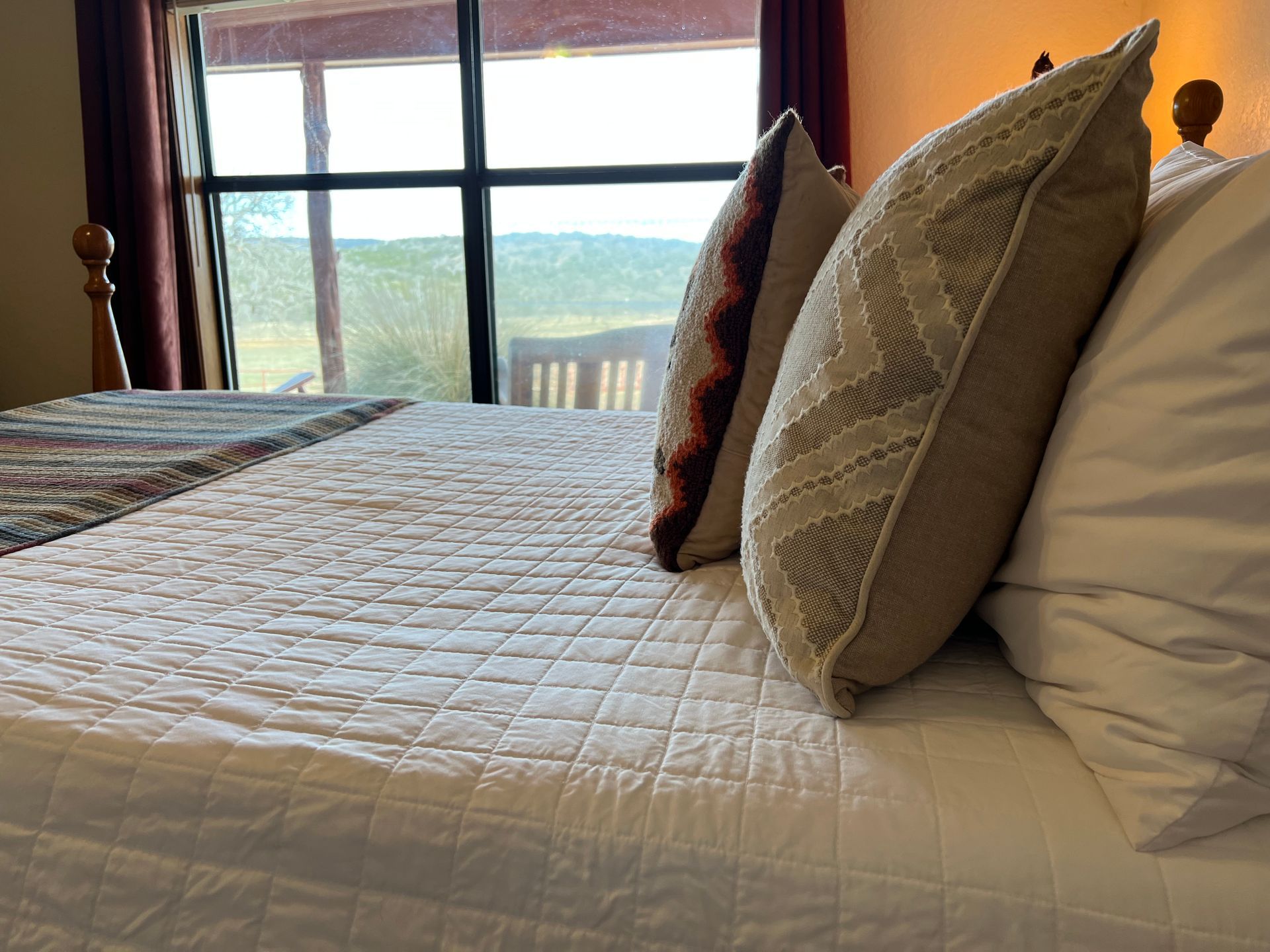 A bed with white sheets and pillows in front of a window.