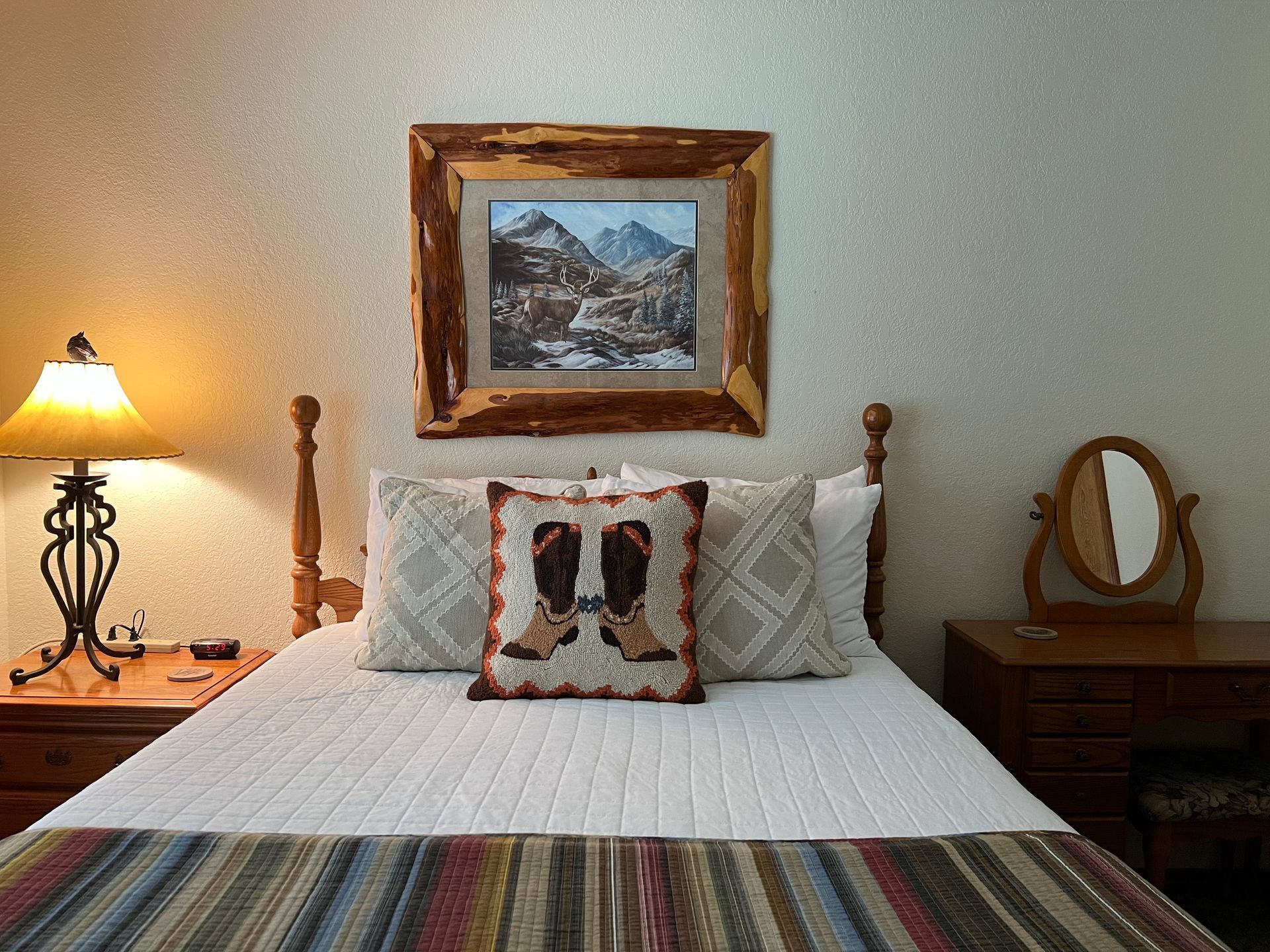 A bedroom with a bed , lamp , mirror and painting on the wall.