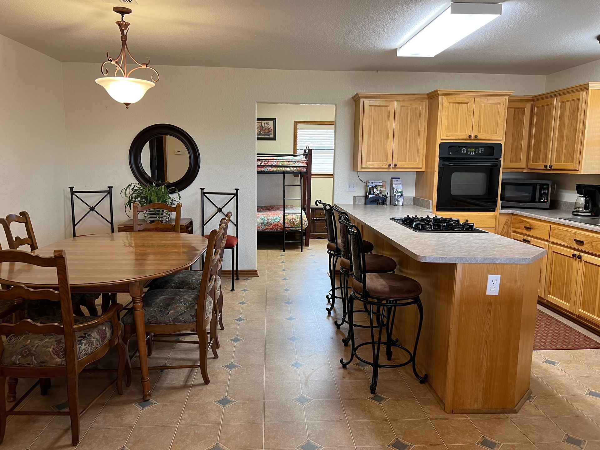 A kitchen with a table and chairs and a bunk bed in the background.