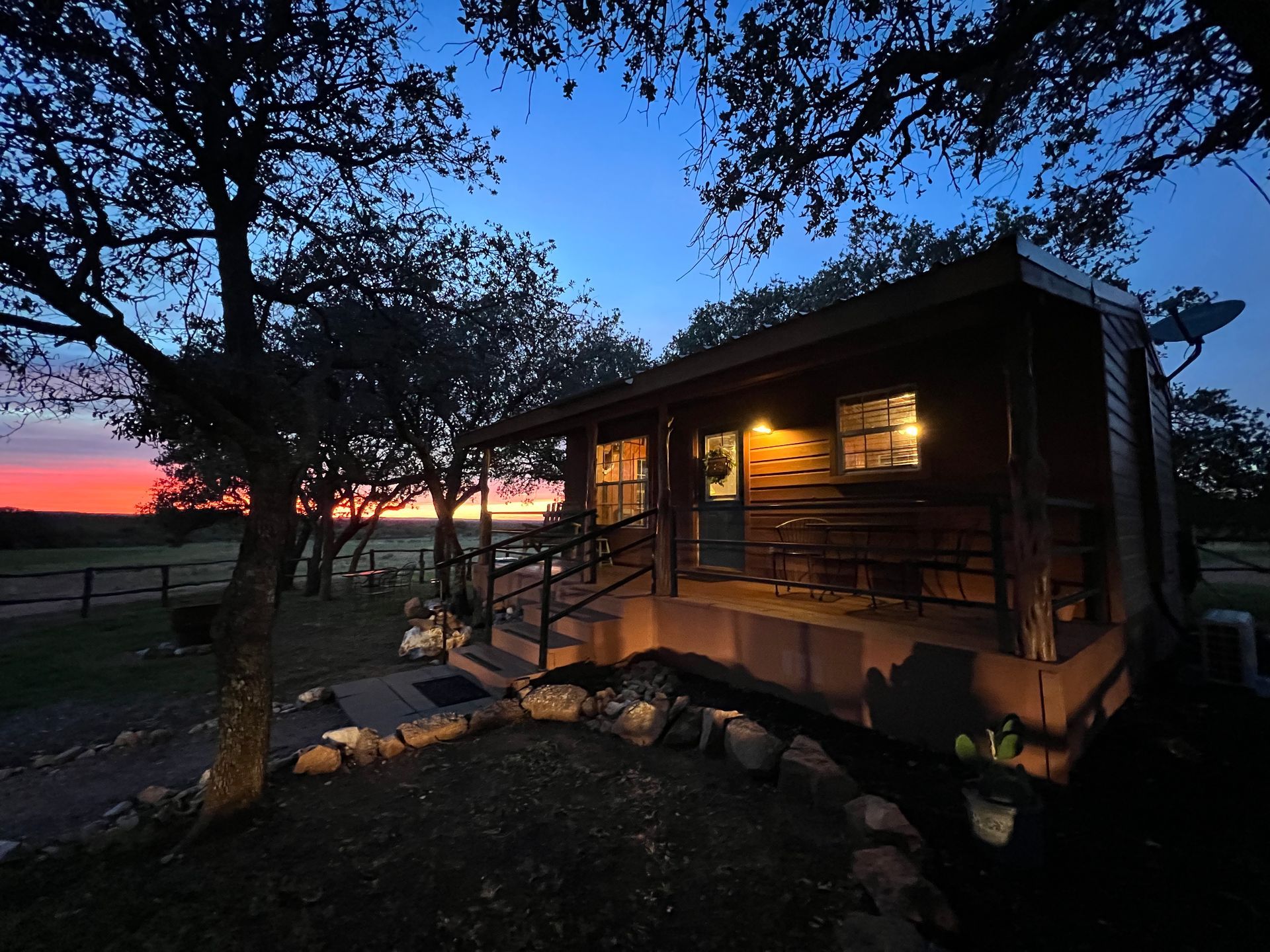 A small cabin is lit up at night with a sunset in the background