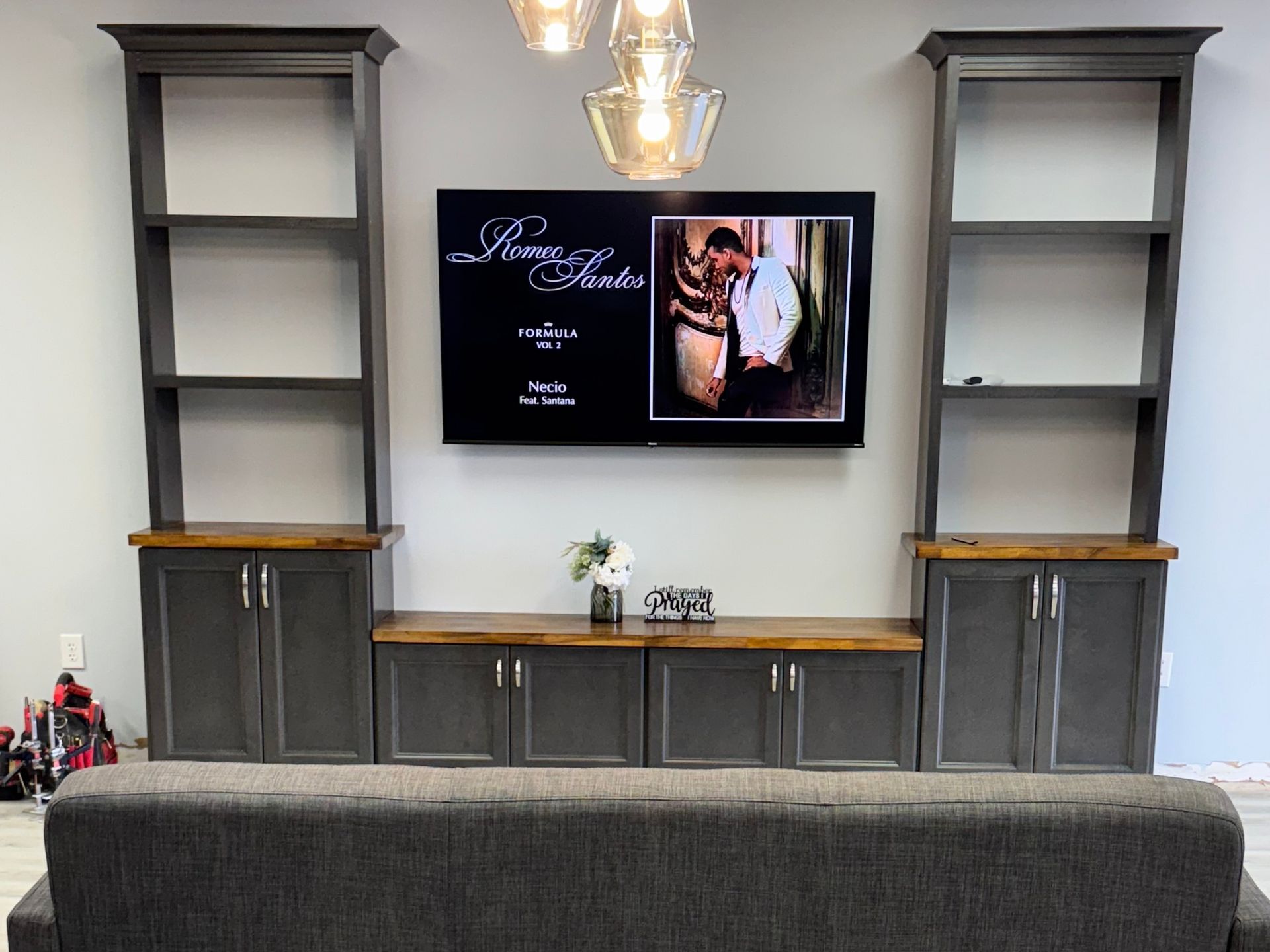 Built-in gray entertainment center with TV, shelves, and cabinets. A sofa is in the foreground.