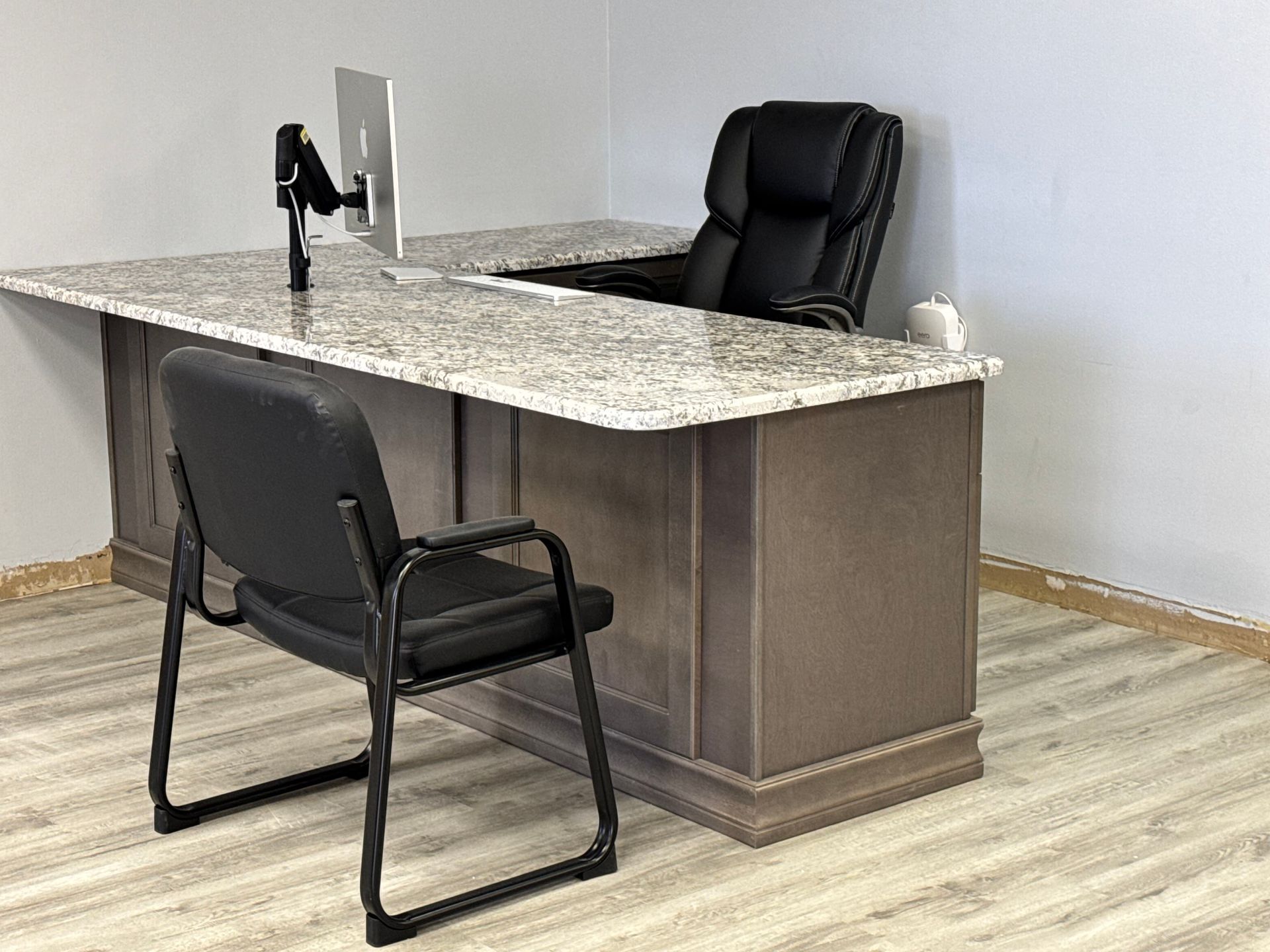 Office desk with granite top, two black chairs, and a computer against a gray wall.