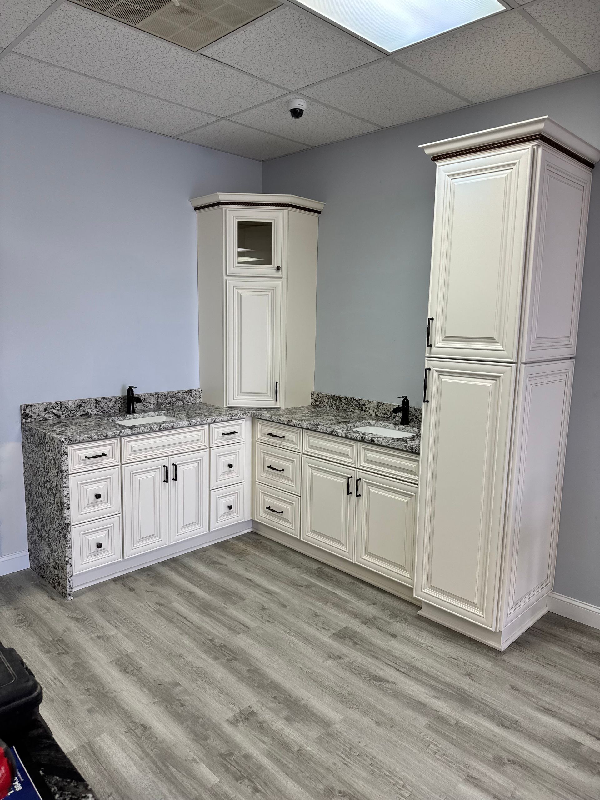 Bathroom with white cabinets, granite countertops, and two sinks. Light blue walls and gray wood-look flooring.