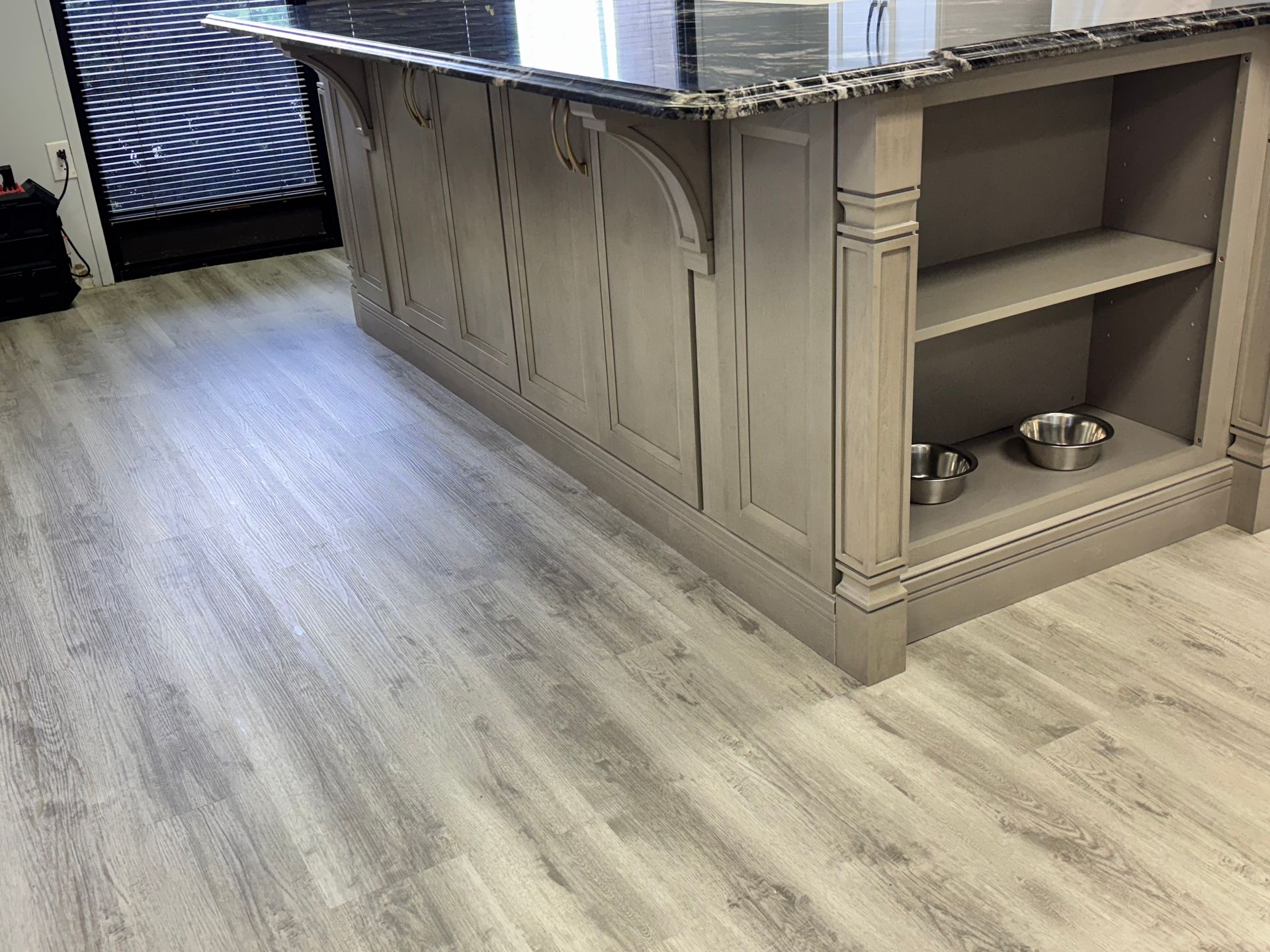 Gray wood-look flooring with a matching kitchen island. The island has shelving and a dark countertop.