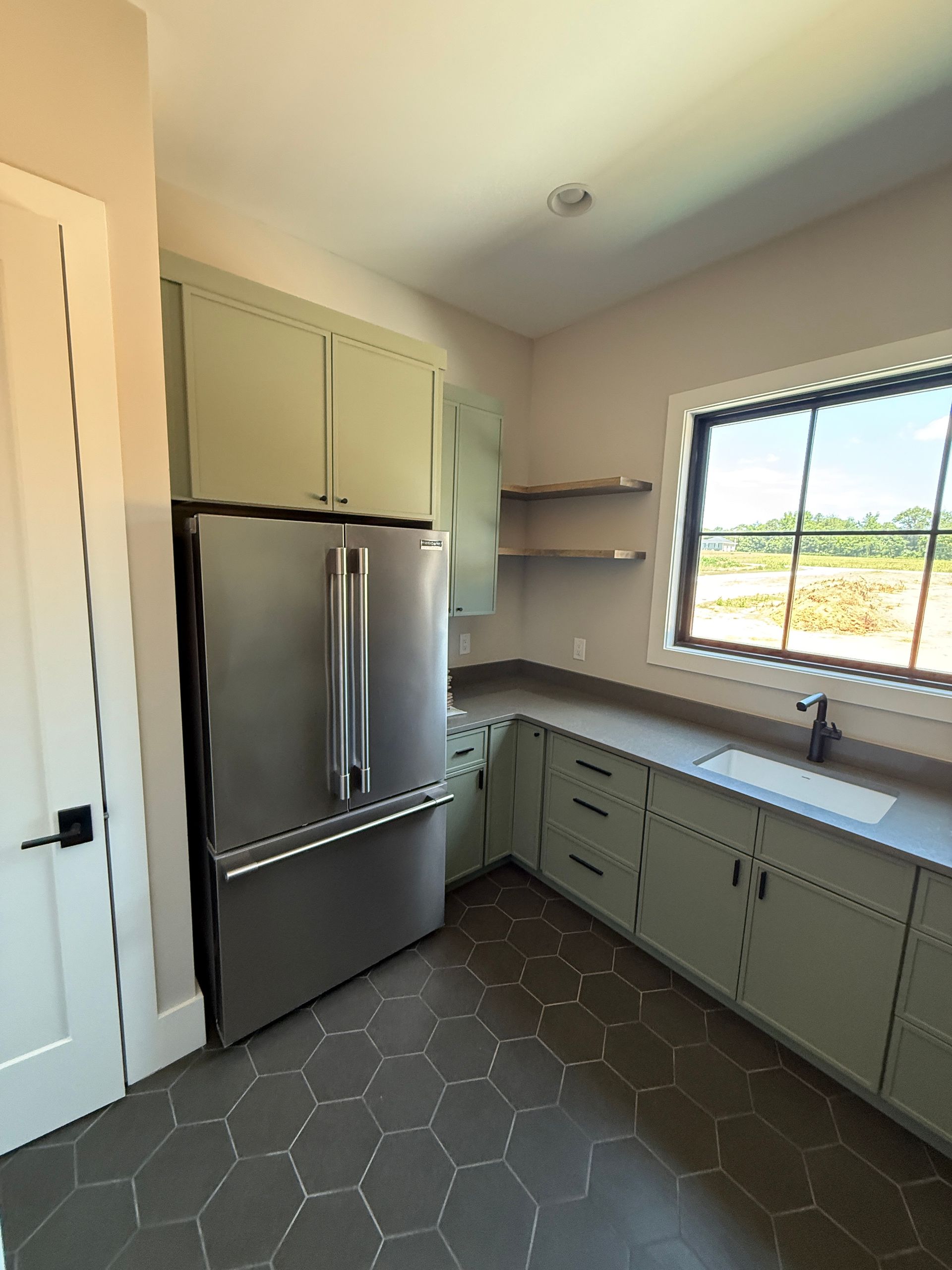 Kitchen with sage green cabinets, stainless steel refrigerator, dark countertops, and hexagonal floor tiles.
