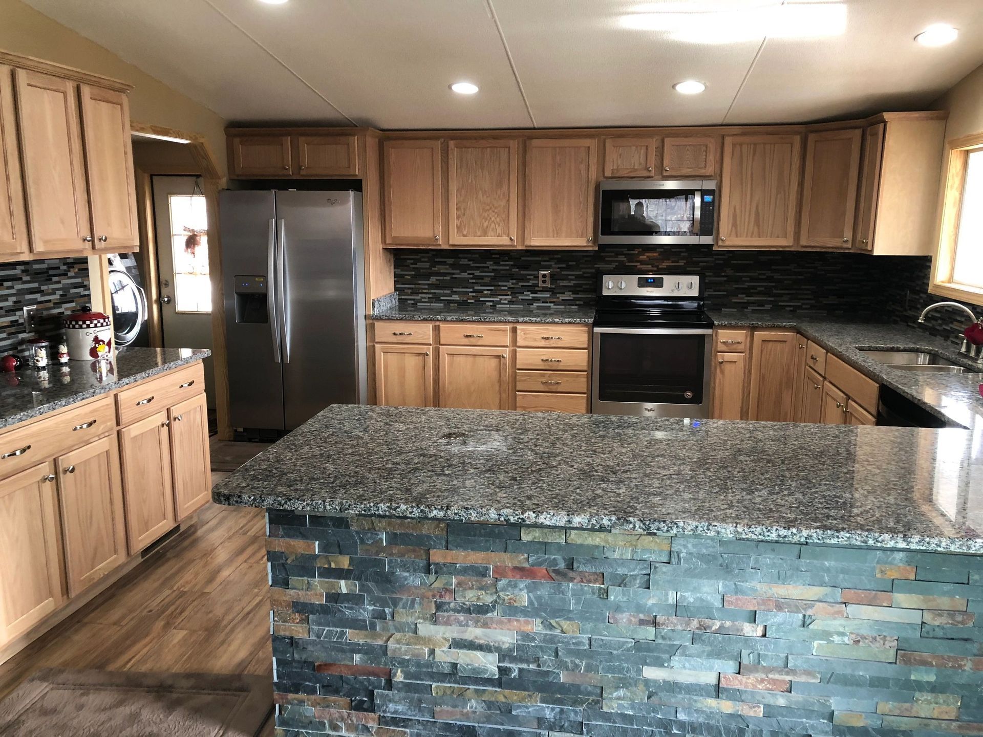 Kitchen with light wood cabinets, granite countertops, and stone-faced island. Stainless steel appliances.