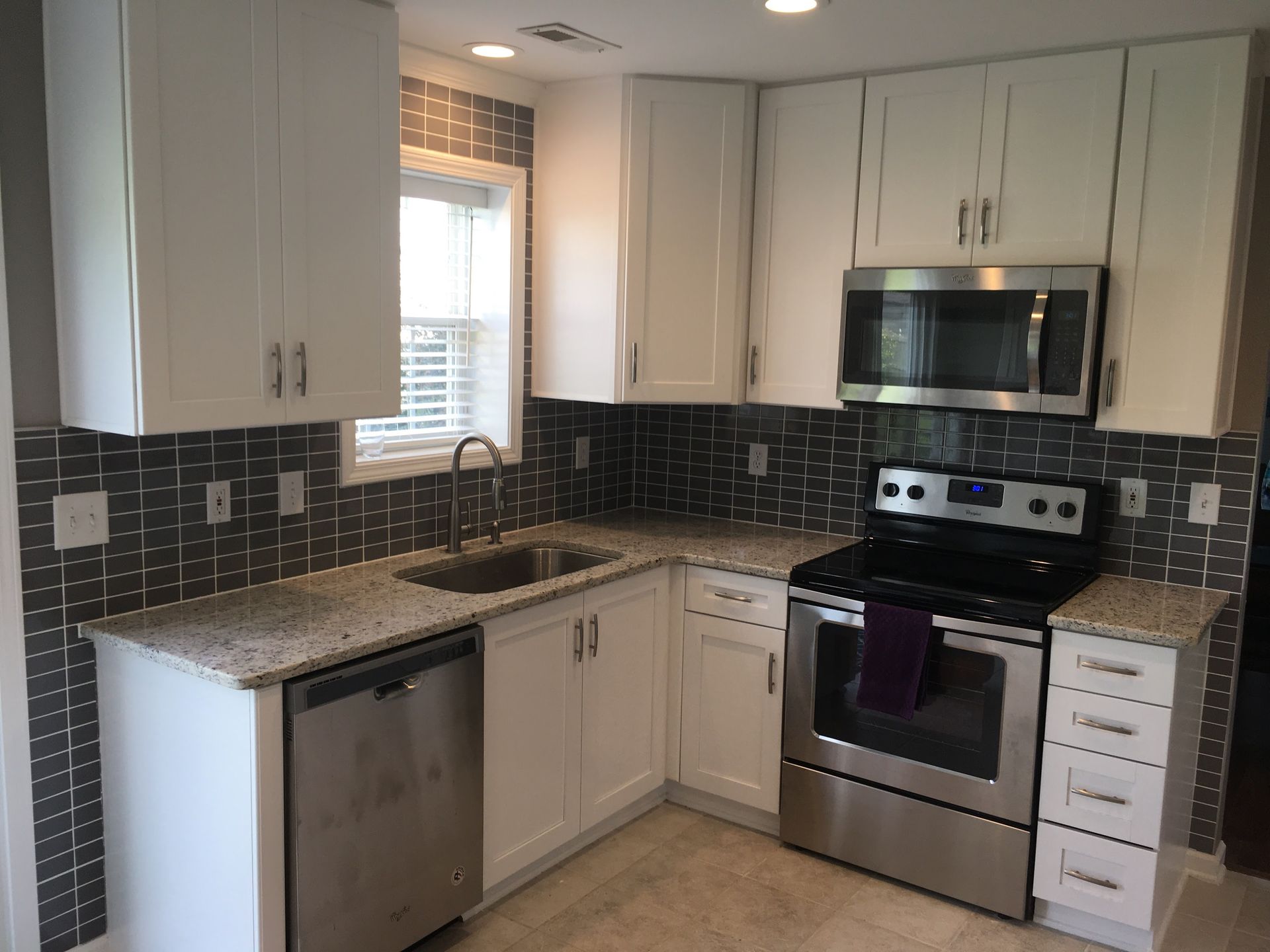 White kitchen with stainless steel appliances, granite countertops, and dark gray tiled backsplash.
