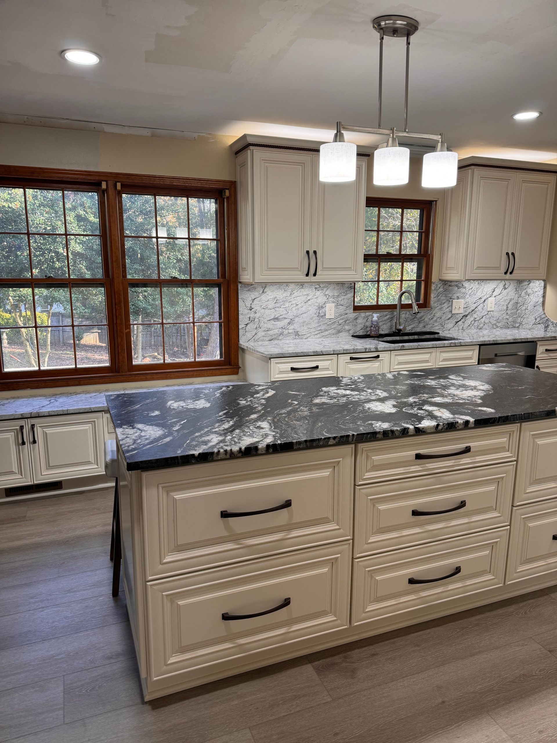 Cream-colored kitchen with an island, dark countertop, and cabinets. Windows with a view.