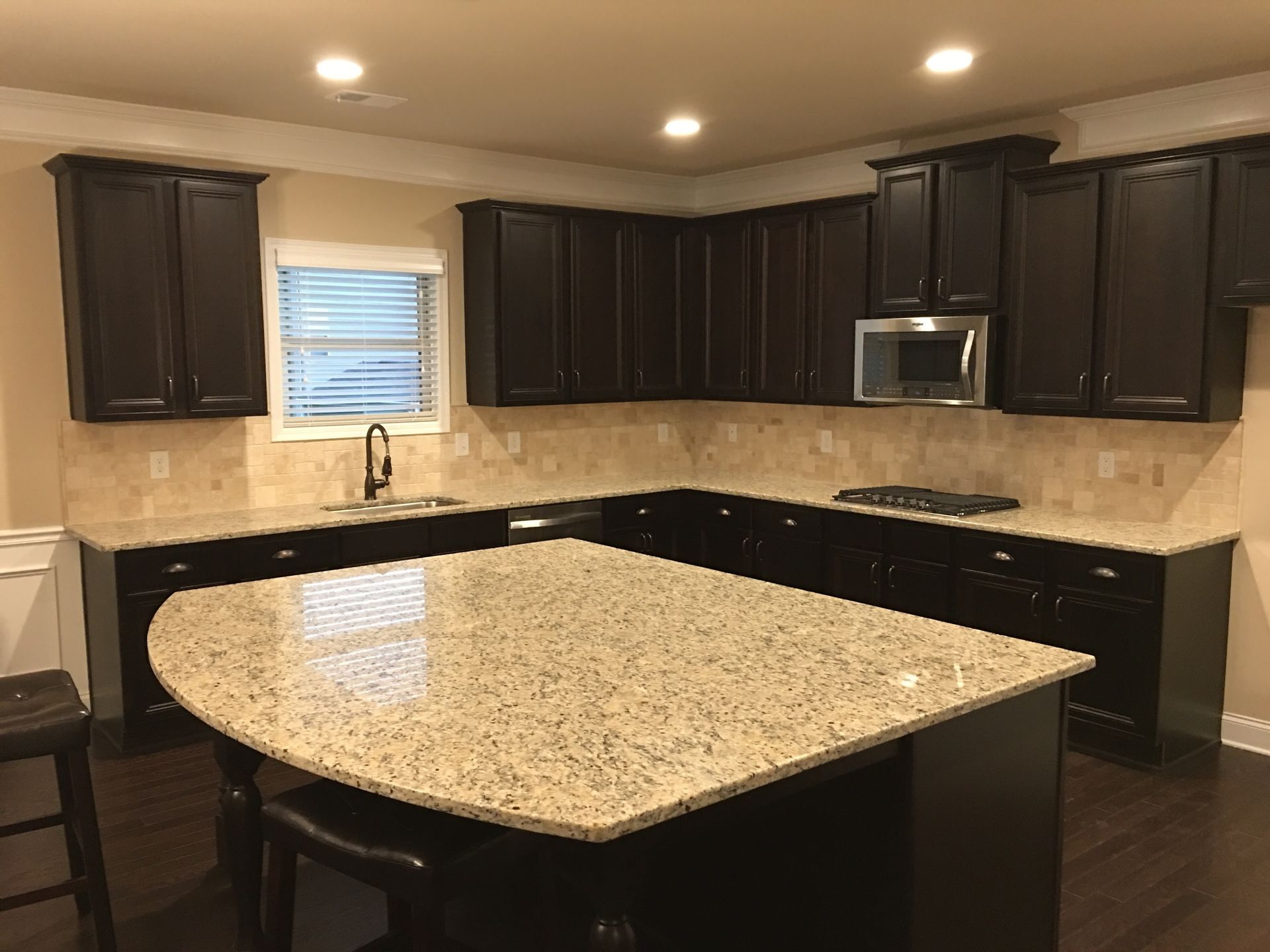 Dark cabinets and granite countertops in a kitchen. Island in the center, microwave above the gas stovetop.