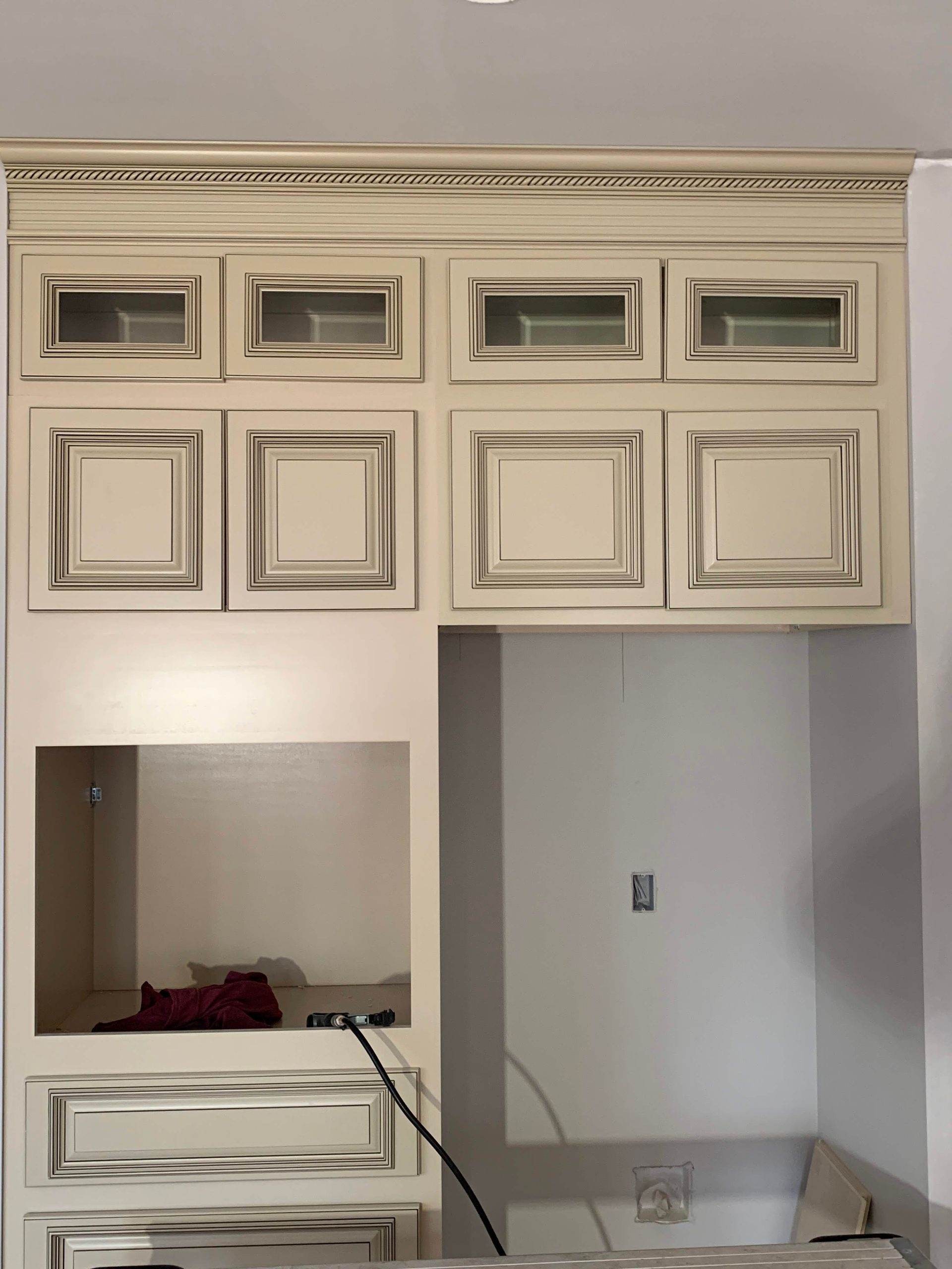 Cream-colored kitchen cabinets with distressed dark edges, above a built-in microwave and drawer space.