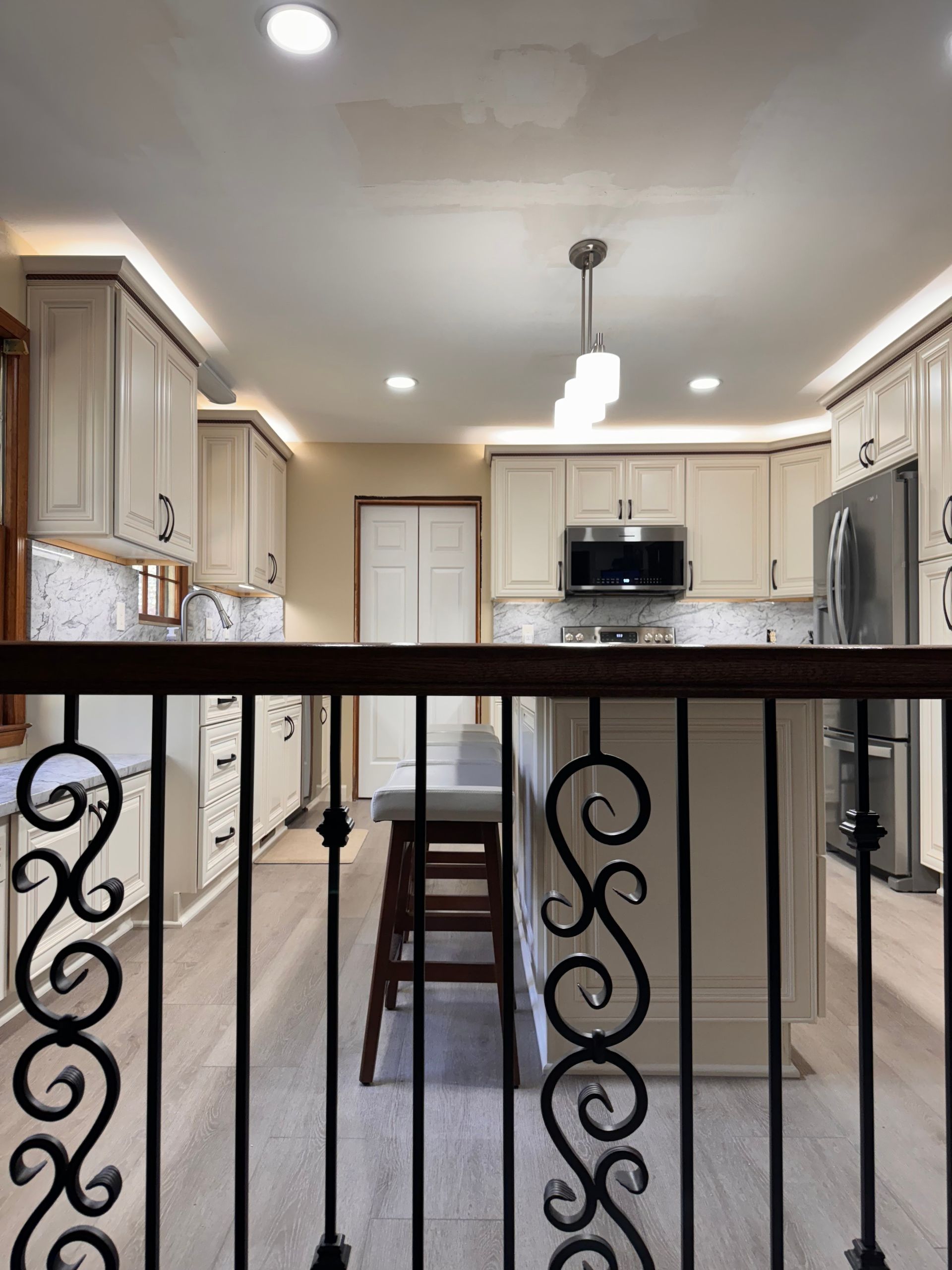 Kitchen interior with light cabinets, stainless steel appliances, and an island. Dark wrought iron railing in the foreground.