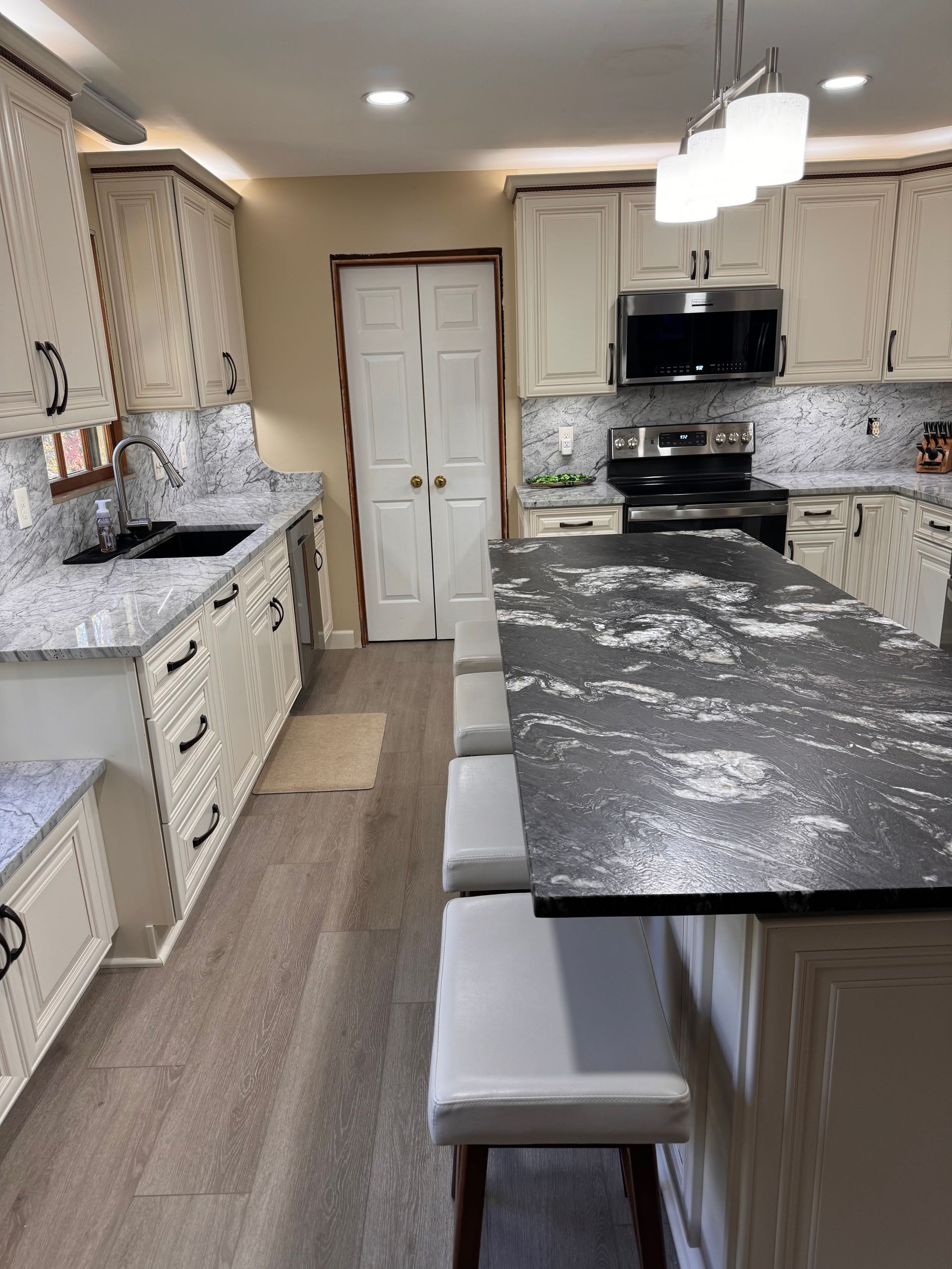 Kitchen with white cabinets, dark countertops, island with seating, and stainless steel appliances.